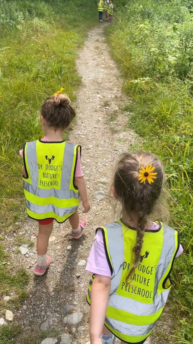 Two children walk a grassy trail, one with a black-eyed susan tucked in her braid