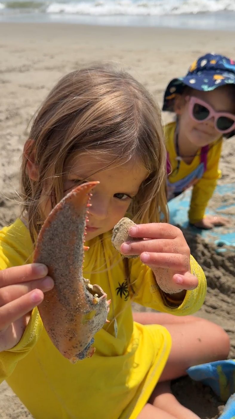 A child holds a lobster claw up to the camera at the beach