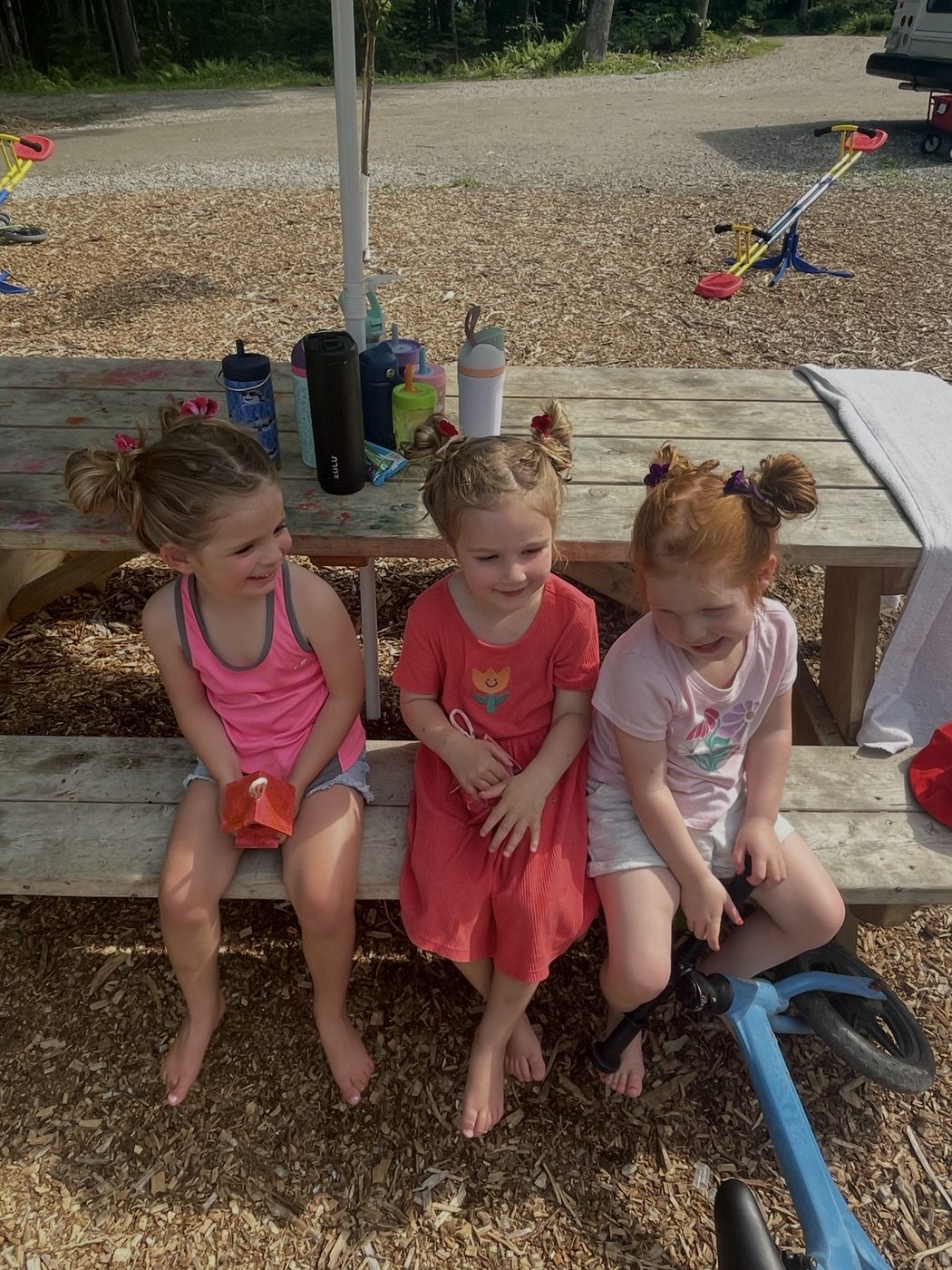 Three friends giggle together on a picnic table bench