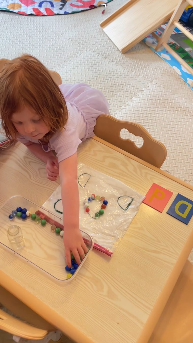 A child traces the letter D by pressing marbles along its shape in a sensory bag