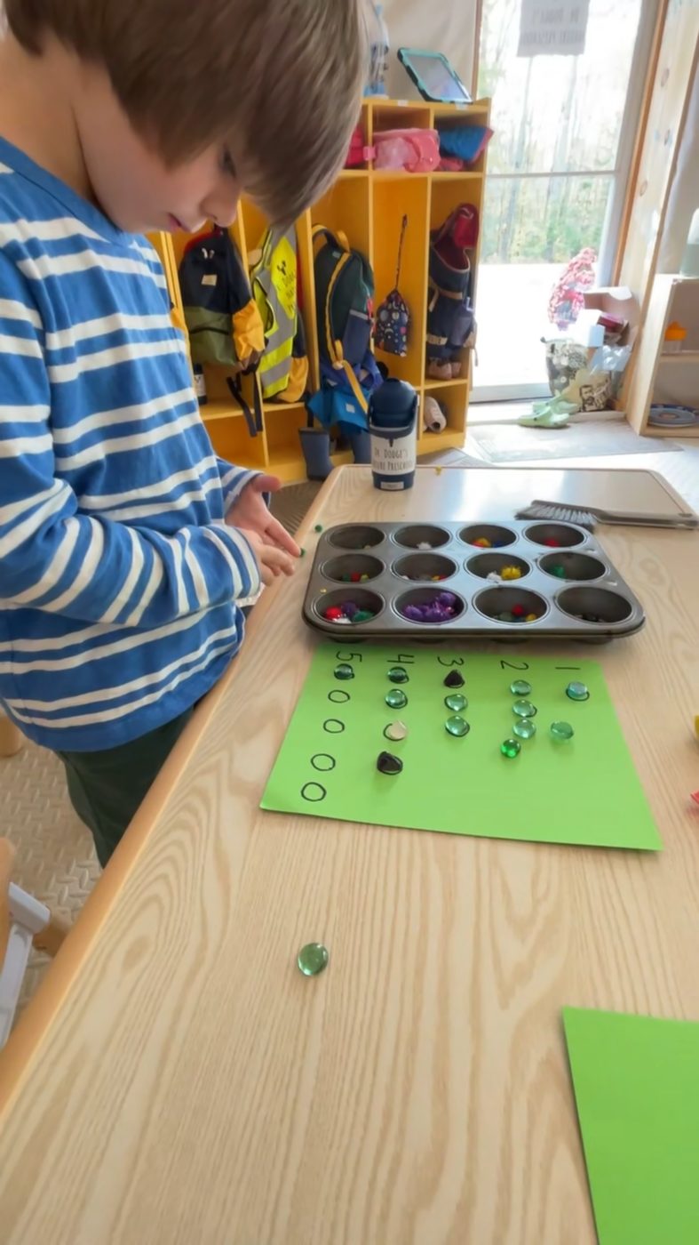 A child counts gems onto a numbered mat beside a muffin-tin sorting tray