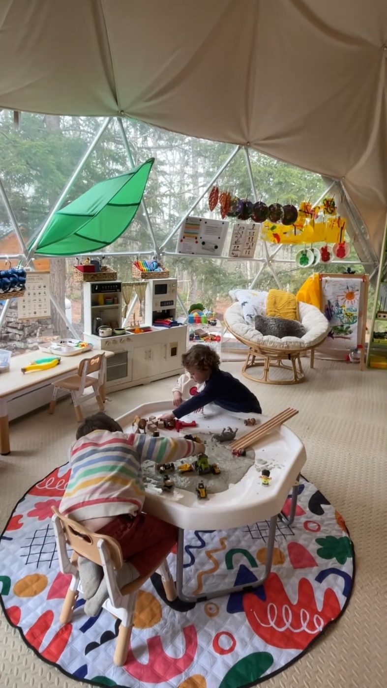 Inside the geodesic dome classroom, children play at a sensory table beneath the canopy