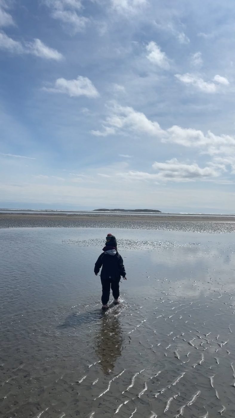 A child in winter layers wanders the tidal flats under a huge Maine sky