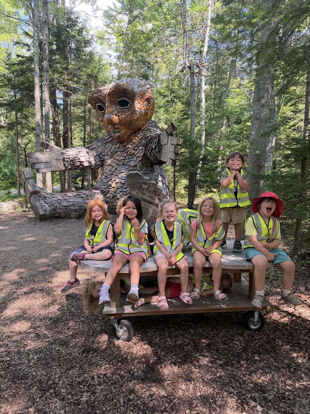 The class poses with a giant wooden troll sculpture in the woods