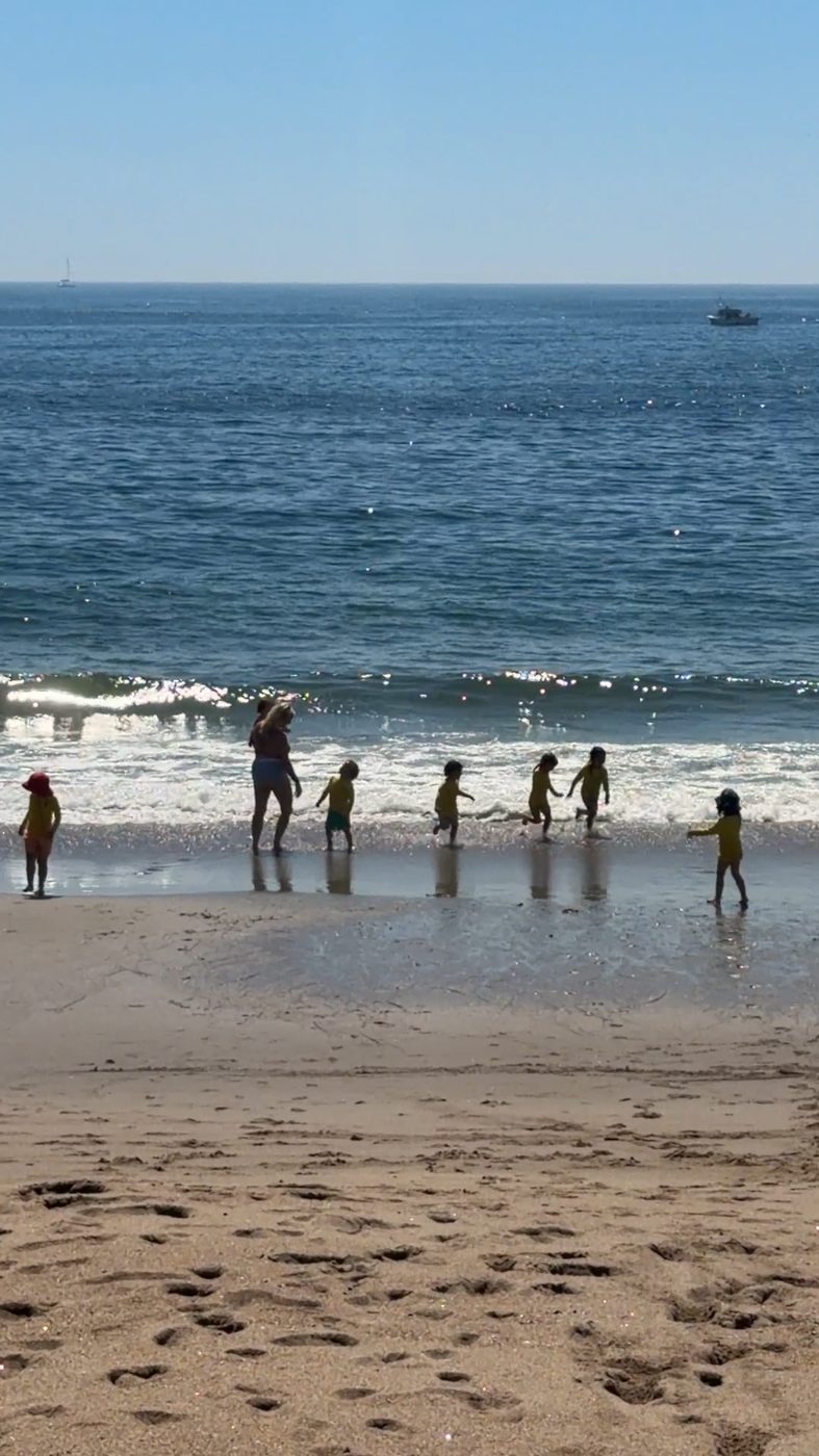 Children run in the waves with a teacher at a sandy beach