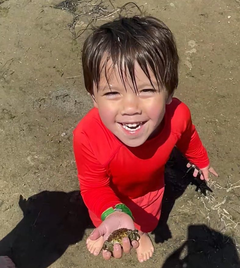 A young child beams while holding a small crab found at the water's edge